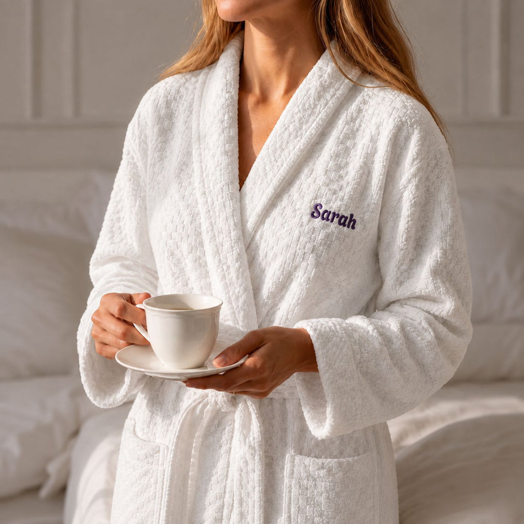 Woman wearing personalized white cotton robe with embroidered name, holding coffee