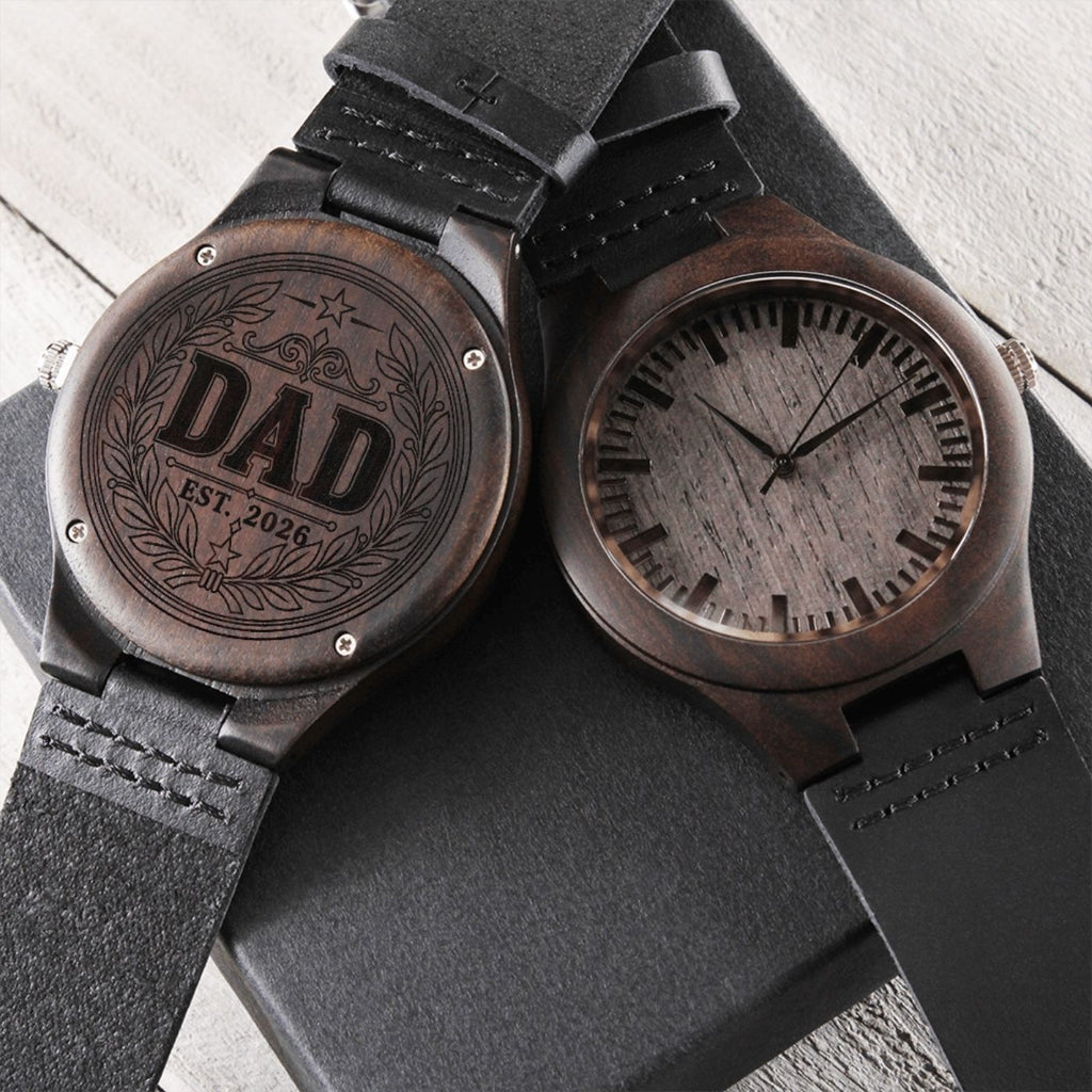 Hand holding an engraved wood watch showing DAD EST 2026 wreath design on the case back